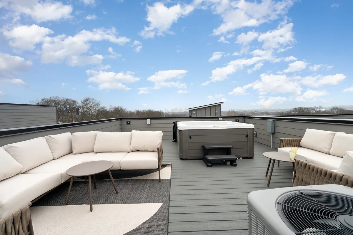 The upper deck of the rooftop patio showcases a luxurious hot tub surrounded by plush lounge seating and contemporary outdoor furniture. The scene is set during sunset, with city lights beginning to glow, emphasizing the panoramic Nashville skyline. The mood is tranquil and indulgent, inviting guests to unwind and soak in the views.