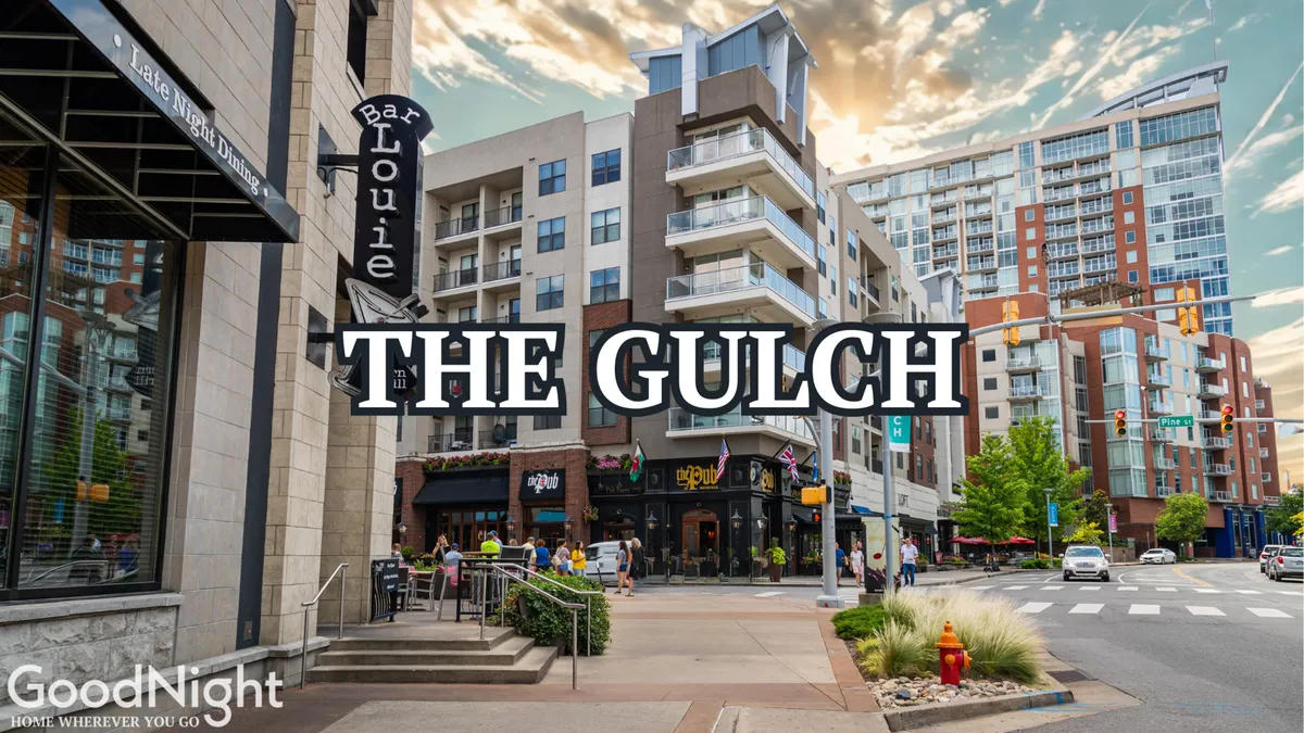A bustling nighttime street scene with people dining outdoors in front of the Bar Louie, apartment buildings rising behind, and a vibrant, energetic atmosphere. The scene suggests lively nightlife and gathering spots near the property.