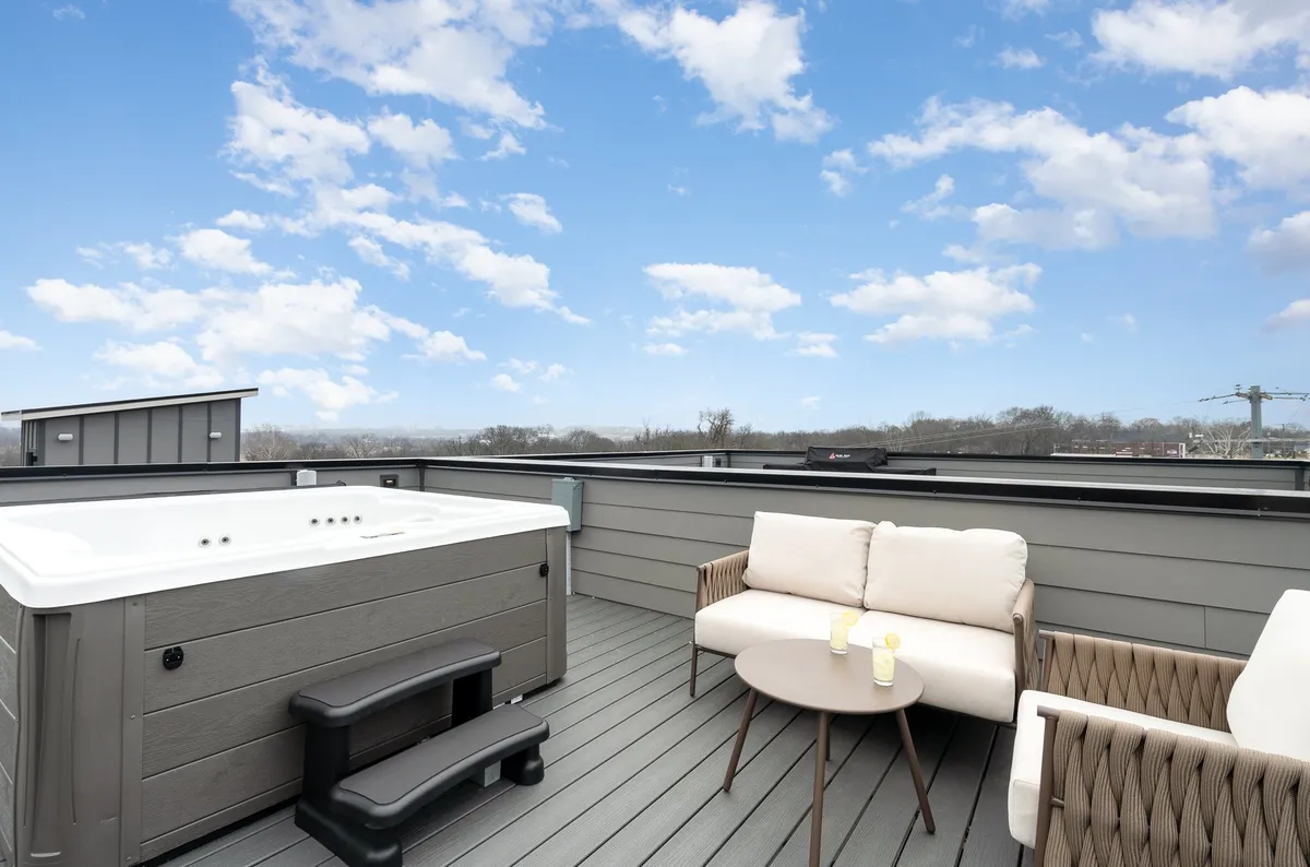 A close-up of the hot tub area on the rooftop, featuring inviting water, comfortable outdoor seating, and a table with drinks prepared for guests. The setting sun casts a golden glow across the deck, enhancing the sense of relaxation and sociability.