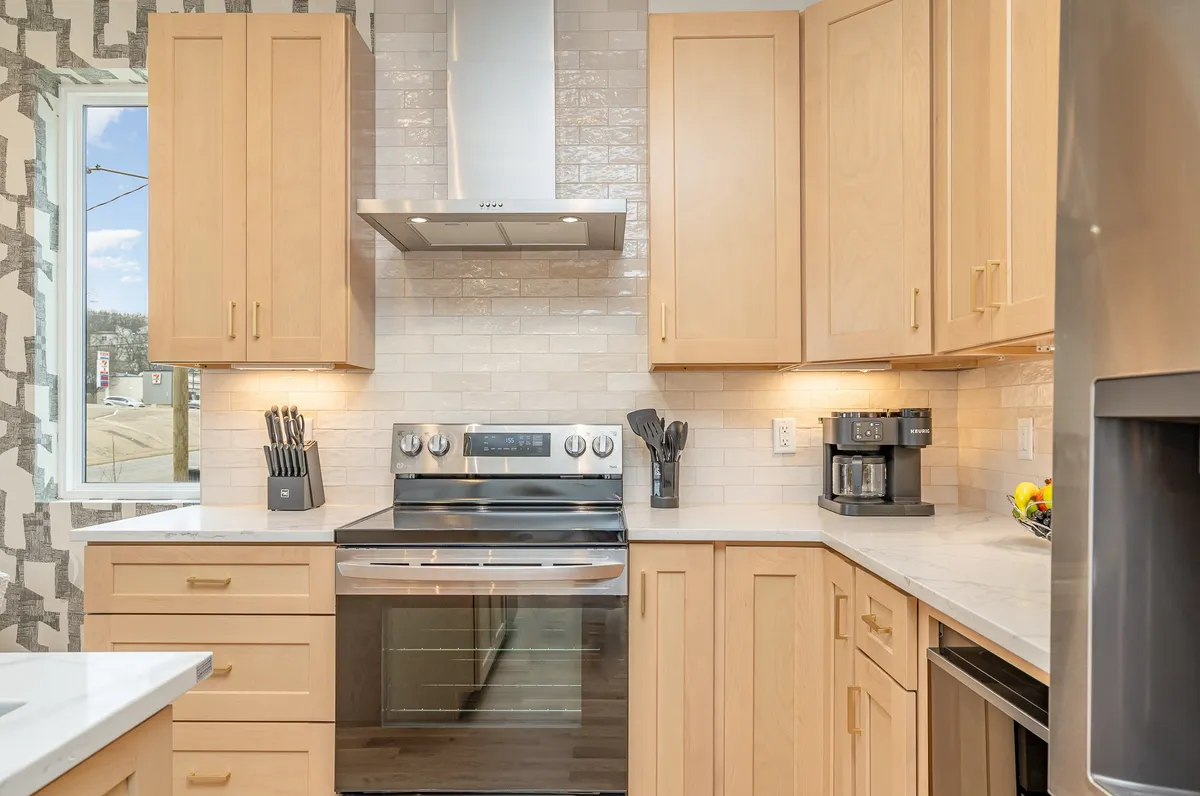 A contemporary kitchen featuring stainless steel appliances, warm wood cabinetry, a spacious countertop, and a window offering natural light. The space is thoughtfully arranged, signaling readiness for guests to enjoy cooking or unpacking groceries upon arrival.