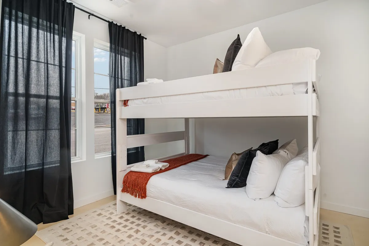A playful bunk room with a queen-over-queen bunk bed, black curtains for privacy, decorative pillows, and a soft rug. The space feels cozy and fun, ideal for kids or extra guests looking for a unique sleep experience.
