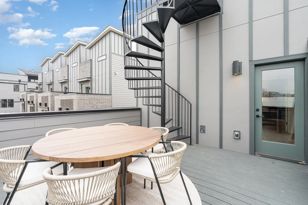 A stylish rooftop patio featuring a spiral staircase, an outdoor dining table, and surrounding city views. The relaxed setting is perfect for unwinding after a night out, suggesting a private oasis just above the pulse of downtown.