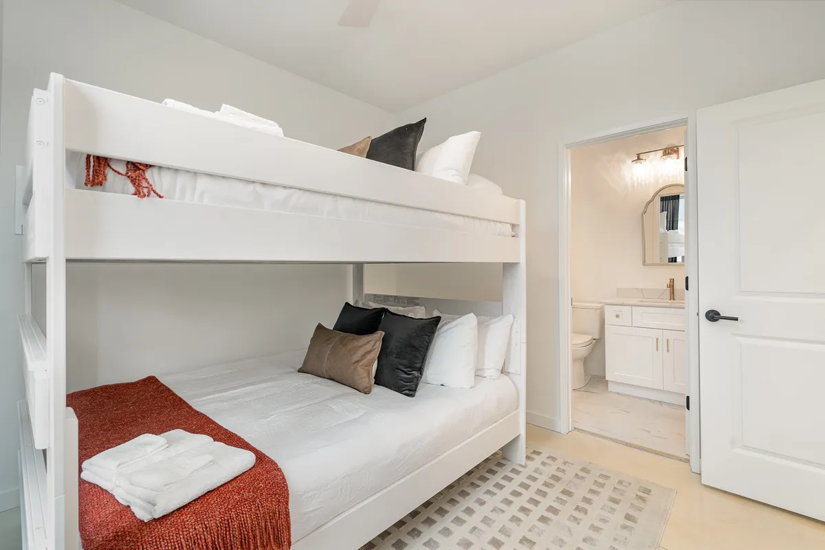 A cozy bunk bed setup with soft lighting, playful decorative pillows, and a view into the bathroom, suggesting a family-friendly and practical living arrangement. The space is approachable and inviting for groups or families with children.