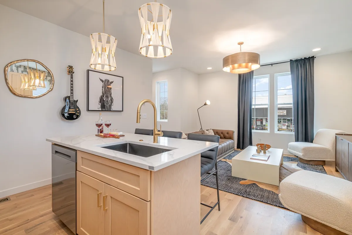 This contemporary space highlights a kitchen island with hanging light fixtures and a sofa arrangement that encourages socializing. Unique Nashville touches, such as a guitar on the wall and local artwork, infuse the space with Music City character. Large windows bring in natural light, enhancing the room’s welcoming feel.